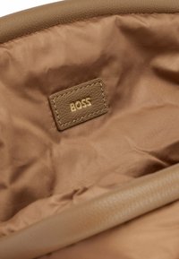 Wnętrze brązowej torby na ramię o gładkiej satynowej teksturze. Posiada jasnobrązową skórzaną metkę wytłoczoną złotymi literami "BOSS".