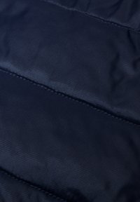 Giacca puffa blu navy in tessuto con una superficie liscia, caratterizzata da sezioni quadrate orizzontali e cuciture a contrasto. Materiale durevole e leggero.