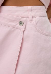 Svetlo rožnate jeans hlače z ravnim pasom in srebrnim gumbom, vidnimi šivi in obliko stranske žepe.