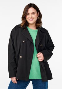 Giacca nera doppiopetto con bottoni argentati, realizzata in un materiale liscio. Abbina con un maglione verde chiaro sotto.