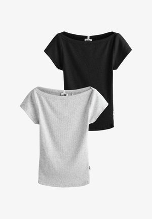 Junge Frau mit lockigem Haar trägt ein hellgraues, eng anliegendes Croptop, blaue Shorts und ein blau gestreiftes Hemd, das um die Taille gebunden ist.