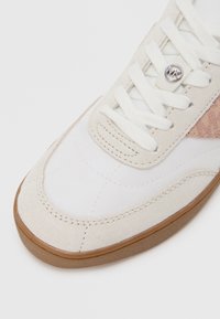 Baskets blanches avec des accents en daim et tissu texturé. Présentent des lacets blancs plats, un logo rond et une semelle en caoutchouc.