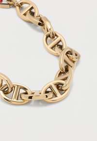 Χοντρό βραχιόλι αλυσίδας από χρυσό με οβάλ κρίκους, που διαθέτει οριζόντιες λεπτομέρειες μπάρας, σε λευκό φόντο.