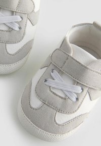 Basket d'enfant grises et blanches avec un dessus en suède et cuir synthétique, des lacets élastiques et une semelle en caoutchouc texturée.