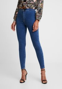 Modré skinny džíny vyrobené z denimu, s vysokým pasem, přiléhavými nohavicemi a zapínáním na knoflík. Ozdobené jemným vyblednutím a prošíváním.