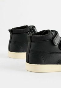 Bottes montantes noires au fini mat, avec une sangle velcro, une semelle en caoutchouc crème contrastante et des détails de couture subtils.