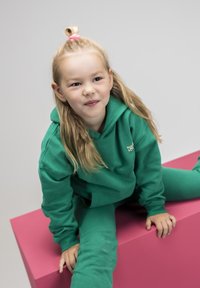 Groene hoodie en bijpassende trainingsbroek van katoen. De hoodie heeft een voorzak en een lichte textuur, met een klein logo op de borst.