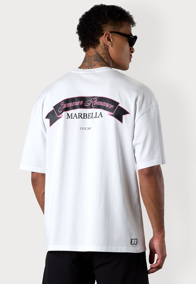 T-shirt blanc surdimensionné avec un graphisme noir et rose au dos portant l'inscription "Summer Romance MARBELLA", à manches courtes et coupe décontractée.