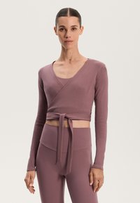 Ribbed, wrap-style top in dusty mauve, with long sleeves and a tie at the waist, paired with high-waisted, matching leggings.