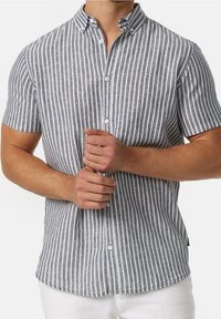 Man in een grijs en wit verticaal gestreept overhemd met korte mouwen die met beide handen een knoop vastmaakt.