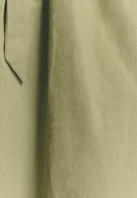 Olivno zeleno blago s rahlo nagubano teksturo, z dolgo, ozko zaponko. Dizajn prikazuje mehki, tekoči slog.