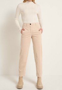 Beiga kordflodpants med sidofickor, rak benpassform och en enkel knappstängning, i kombination med en ljus ribbad långärmad topp.