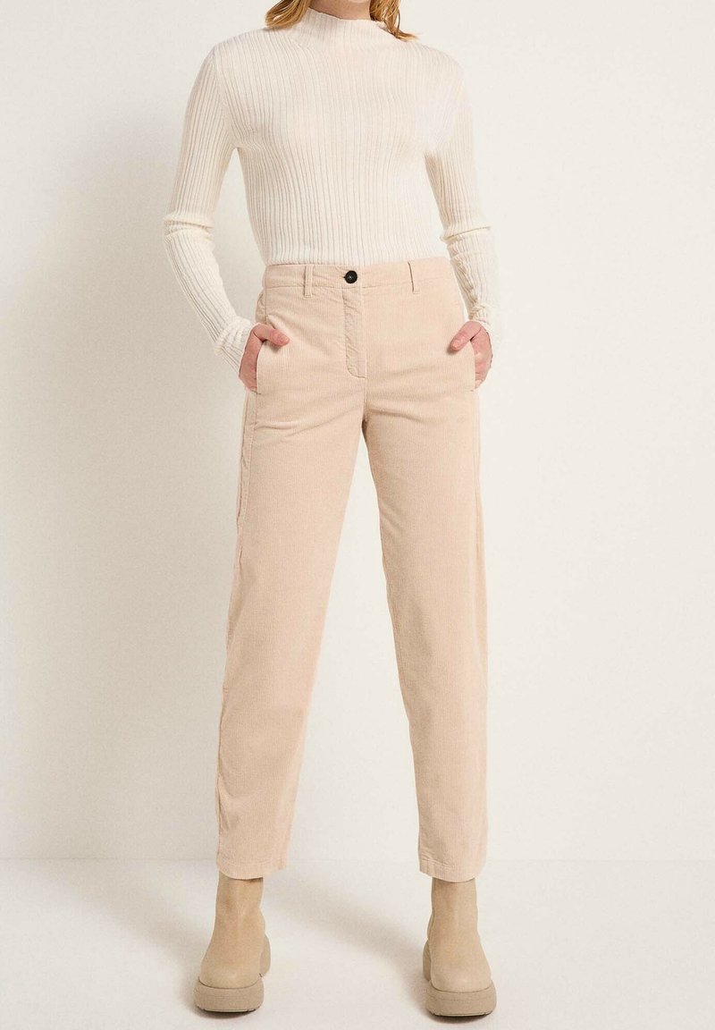 Beiga kordflodpants med sidofickor, rak benpassform och en enkel knappstängning, i kombination med en ljus ribbad långärmad topp.