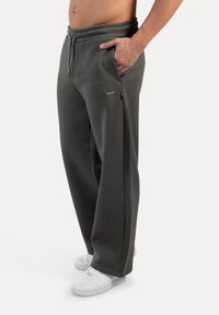 Grå sweatpants lavet af blødt stof, med elastisk talje, sidelommer og en løs pasform. Parret med hvide sneakers.