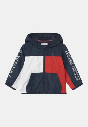 Chaqueta con capucha para niños con cremallera, en azul marino, blanco y rojo, con bolsillos delanteros y el texto "TOMMY JEANS" impreso en ambas mangas.