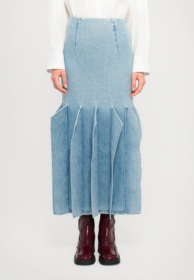 Lyseblå denimnederdel med en flagrende design, der har store folder og lommer. Knælængde, parret med blanke burgunder ankelstøvler.