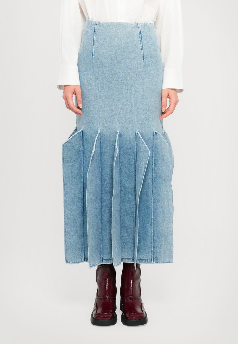 Gonna di jeans blu chiaro con un design svasato, caratterizzata da ampie pince e tasche. Lunghezza al ginocchio, abbinata a stivali alla caviglia bordeaux lucidi.