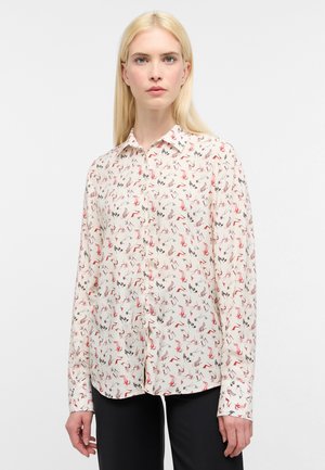 Camicia bianca con bottoni, decorata con un motivo floreale in rosso, rosa e nero. Maniche lunghe, colletto e una texture liscia.