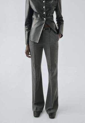 Black leather jacket with silver buttons, paired with gray wide-leg trousers and black heeled shoes, showcasing a tailored fit.