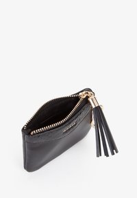 Piccola moneta porta monete in pelle nera con cerniera dorata, tirante con nappina e la scritta "MIRIADE" in rilievo sul davanti.