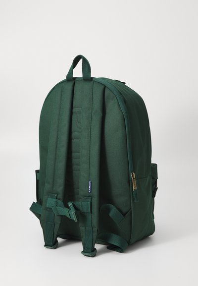 Mochila de tela verde con un diseño redondeado, correas ajustables y acolchadas, asa superior, bolsillo frontal con cremallera y compartimentos de malla en los laterales.