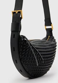 Svart läderväska med en texturerad yta som har upphöjda triangulära mönster, ett spänne i guldton och en justerbar rem.