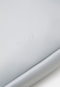 Prodotto Rains di colore grigio chiaro, con una texture liscia e opaca, caratterizzato da un marchio in rilievo. Design minimalista con bordi curvi.