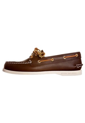 Chaussure bateau en cuir marron avec coutures blanches, lacets couleur fauve et semelle en caoutchouc blanche, vue de profil.