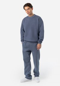 Afslappet outfit med en blå sweatshirt og matchende sweatpants, lavet af blødt stof med en afslappet pasform. Hvide sneakers fuldender looket.