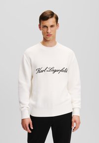 Kremo spalvos megztinis, su tekstūruotu mezgimo raštu ir įribuotomis rankovėmis bei apykakle. Priekyje juodas siuvinėtas "Karl Lagerfeld" logotipas.