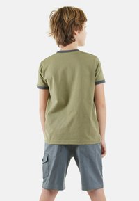 Camiseta verde oliva con mangas cortas en gris, combinada con pantalones cortos cargo grises que tienen bolsillos frontales y laterales.