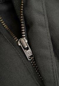 Black zipper details on textured fabric, featuring a YKK pull tab, with metal teeth visible along one side and stitched edge.