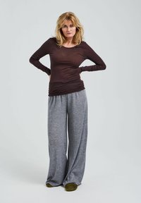 Brun långärmad åtsittande topp i kombination med grå vida byxor. Toppens tyngd är lätt; byxorna har en mjuk textur och elastiskt midjeband. Gröna skor.