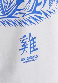 Vit t-shirt med blå grafisk design som har stiliserade element och kinesiska tecken, samt texten "ORIGINALS WORLDWIDE."