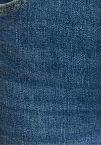 Denim fabric in medium blue, featuring a subtle texture and classic weave. Exposed stitching in a contrasting golden hue along the edge.