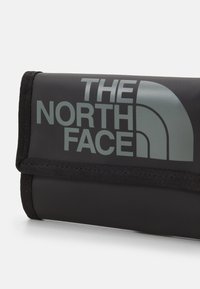 Svart rullbar oppbevaringspose laget av holdbart materiale, med en stor grå logo av "The North Face" og en teksturert overflate.