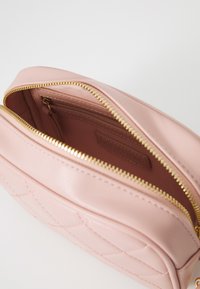 Bolsa de maquilhagem em pele rosa com design matelassé, fecho dourado e bolso interior forrado. Apresenta uma textura suave e uma forma estruturada.
