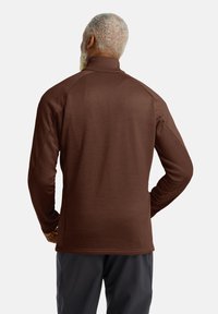 Brauner Langarm-Pullover mit Stehkragen, der eine glatte Textur und Raglanärmel aufweist, kombiniert mit dunklen minimalistischen Hosen.