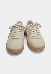 Paire de baskets en daim beige avec lacets blancs et semelles en caoutchouc gomme, vues de face sur fond blanc.
