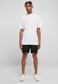 Hvit kortermet skjorte med glidelås laget av bomull, kombinert med svarte shorts og hvite joggesko. Passformen er avslappet og uformell.