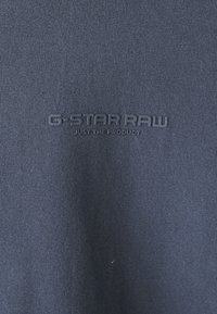 Cămașă din bumbac de culoare bleumarin, cu textură ribbed și logo-ul în relief "G-STAR RAW" cu "JUST THE PRODUCT" dedesubt, poziționat central.