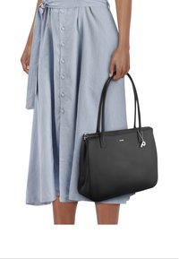 Zwarte leren totebag met een gladde textuur, versterkte handgrepen en zilverkleurige accessoires, vastgehouden door een persoon die een lichtblauwe knop-down rok draagt.