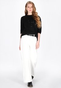 Sorte striktrøje med et struktureret mønster, trekvartlange ærmer, sat sammen med hvide bredbenede bukser og sorte snørebodstøvler.