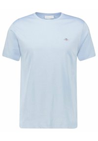 Světle modré bavlněné tričko s krátkými rukávy, kulatým výstřihem a malou vyšitou nášivkou na hrudi. Hladká struktura, volný střih.