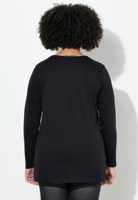 Zwart T-shirt met lange mouwen van zachte stof, voorzien van een ronde hals en een iets langere zoom aan de achterkant. Naadloos ontwerp zonder zichtbare logo's of patronen.