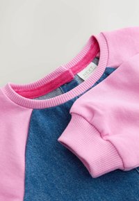 Krátký rukávový top s růžovým žebrovaným límcem a manžetami, s hlavní látkou v modrém denimu. Štítek je viditelný na zadním výstřihu.