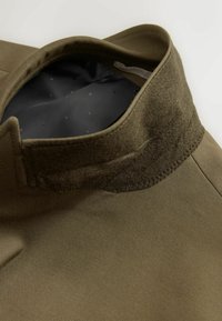 Olīvu zaļš pielāgots žakets ar mīkstu vilnas apkakli, gludu iekšējo odere un precīziem šuvuma elementiem. Iespējas strukturēta dizaina.