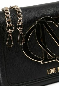 Borsa a tracolla in pelle nera con una brillante catena dorata, grande dettaglio del logo e il testo "LOVE ME" impresso sul davanti.