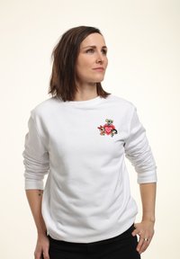 Sudadera blanca con un colorido diseño bordado de tres personajes de dibujos animados y un corazón en el lado izquierdo del pecho. Mangas largas, corte relajado.