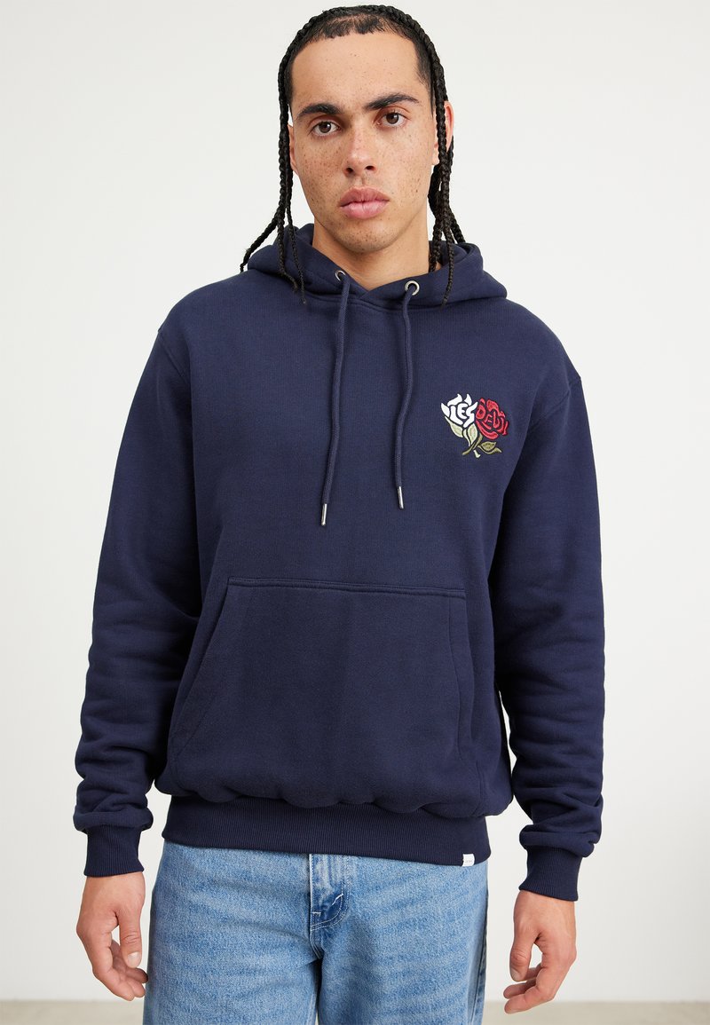 Sudadera azul marino con un bolsillo frontal, capucha con cordón y diseño de rosa bordado en rojo y blanco en el pecho. Tejido suave y texturizado.